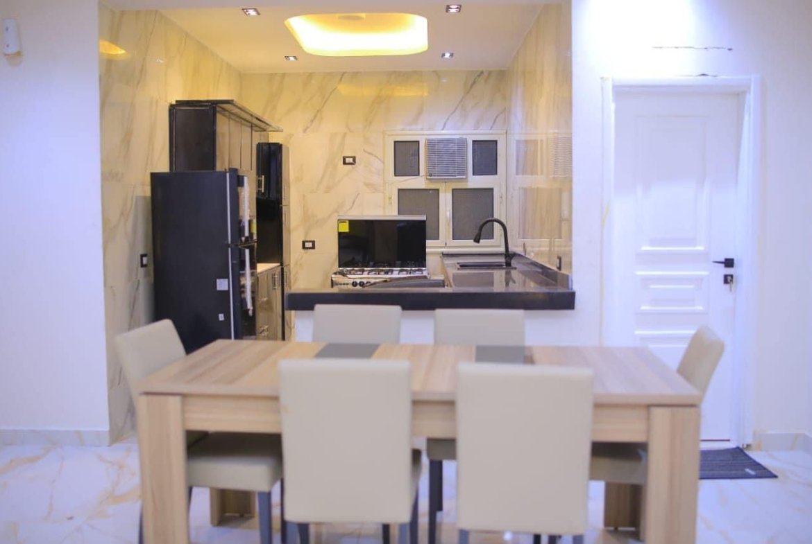 Dining table with cream chairs and an open kitchen behind - apartment in El Yasmeen 1, New Cairo