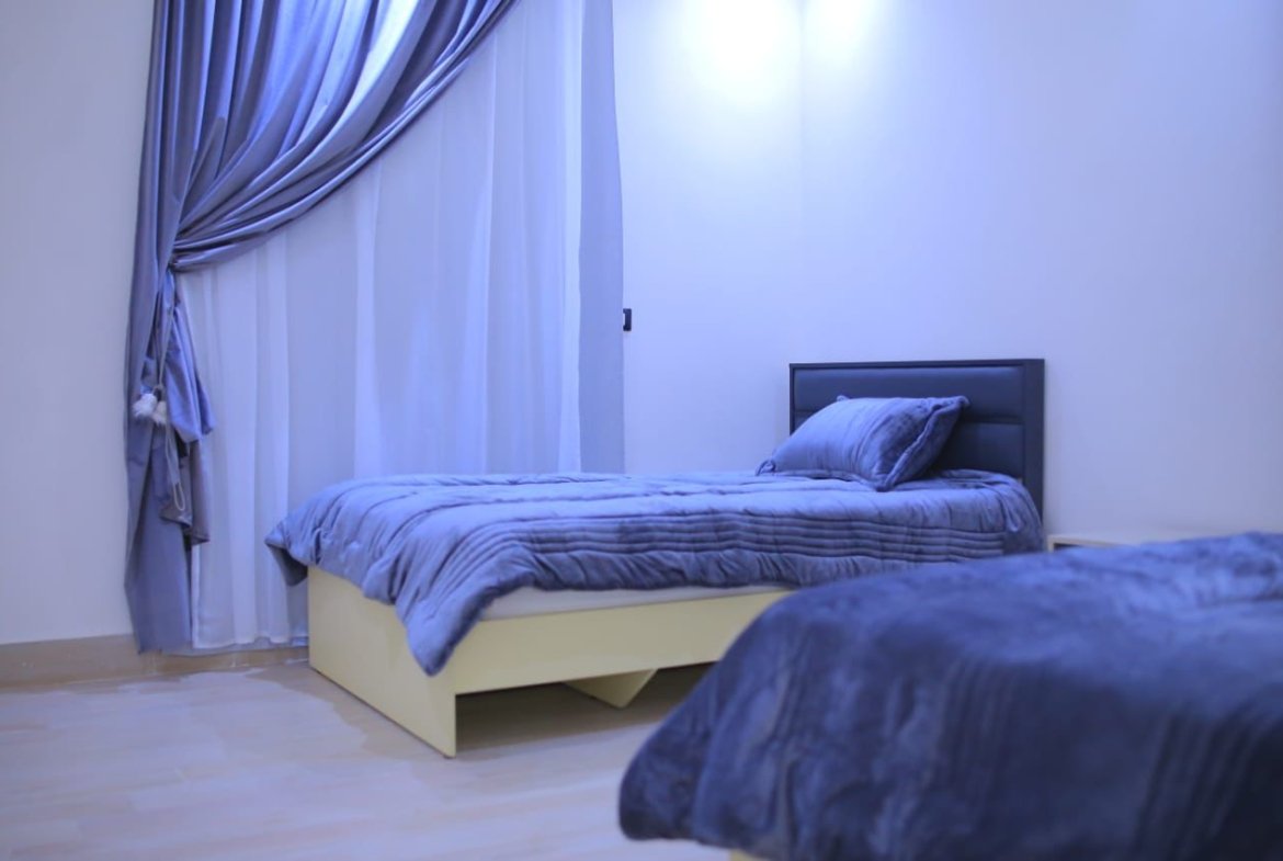 Single bed with a grey headboard and navy blanket beside curtains - apartment in El Yasmeen 1, New Cairo