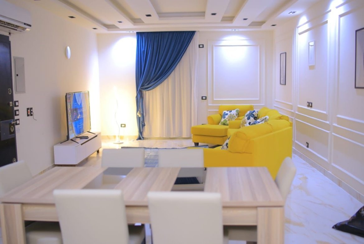 Dining table and yellow sofas beneath a blue curtain - apartment in El Yasmeen 1, New Cairo