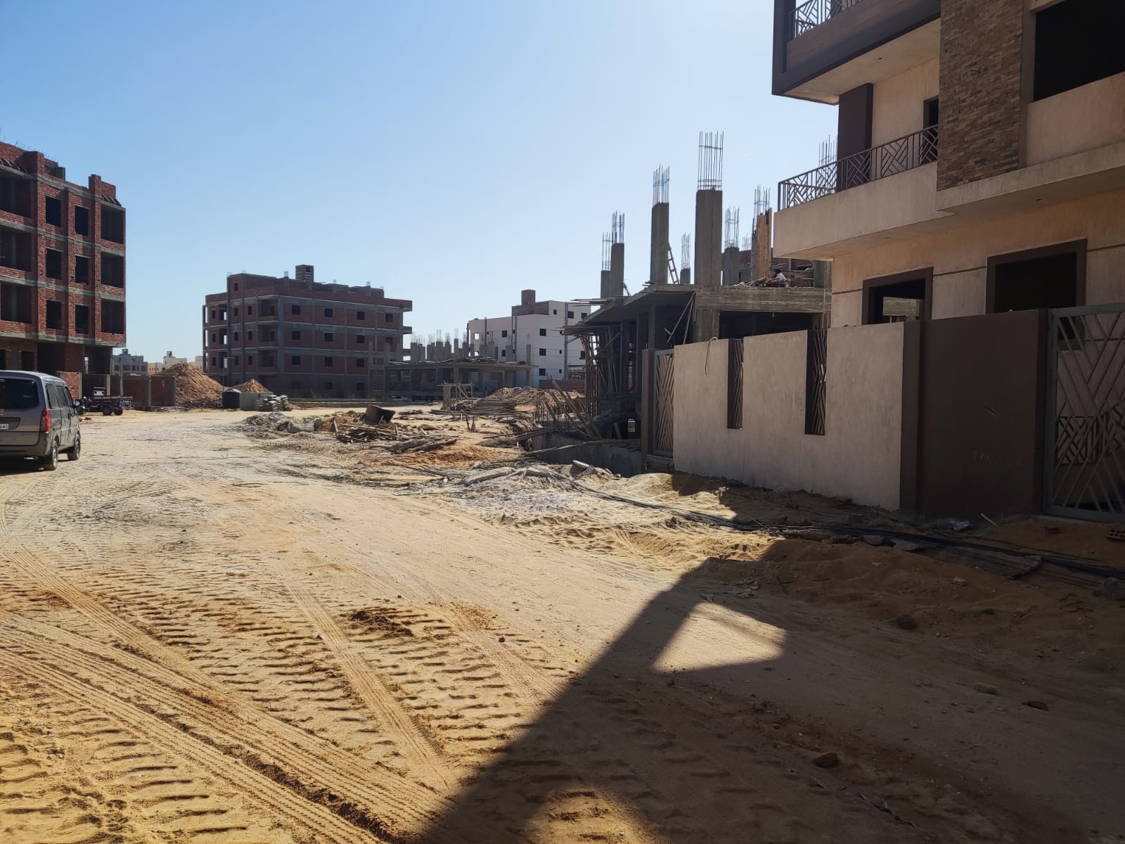 Unpaved street beside a finished building and construction sites - apartment in Beit El Watan, New Cairo