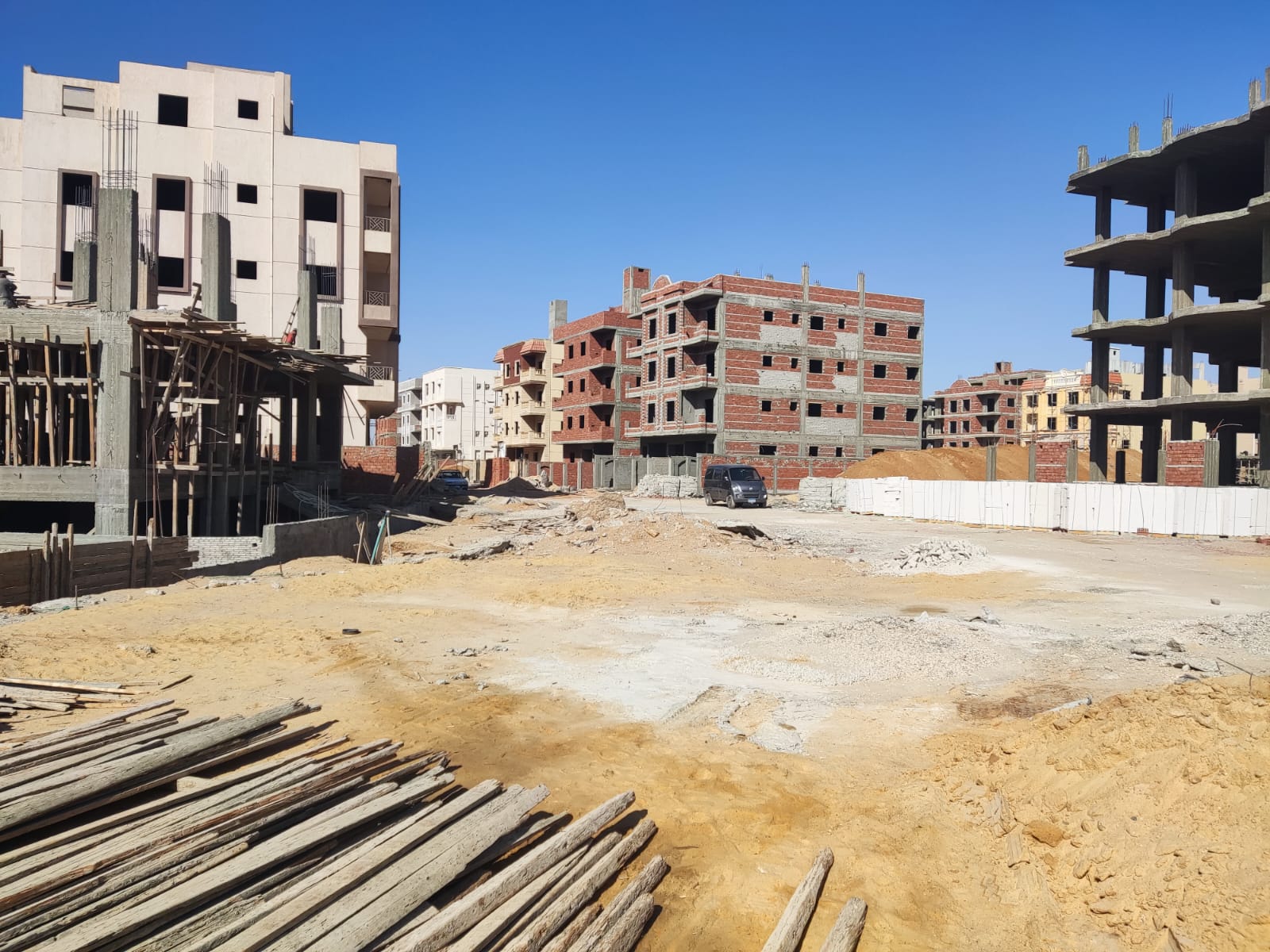 Sandy lot with stacked timber beside residential blocks - apartment in Beit El Watan, New Cairo