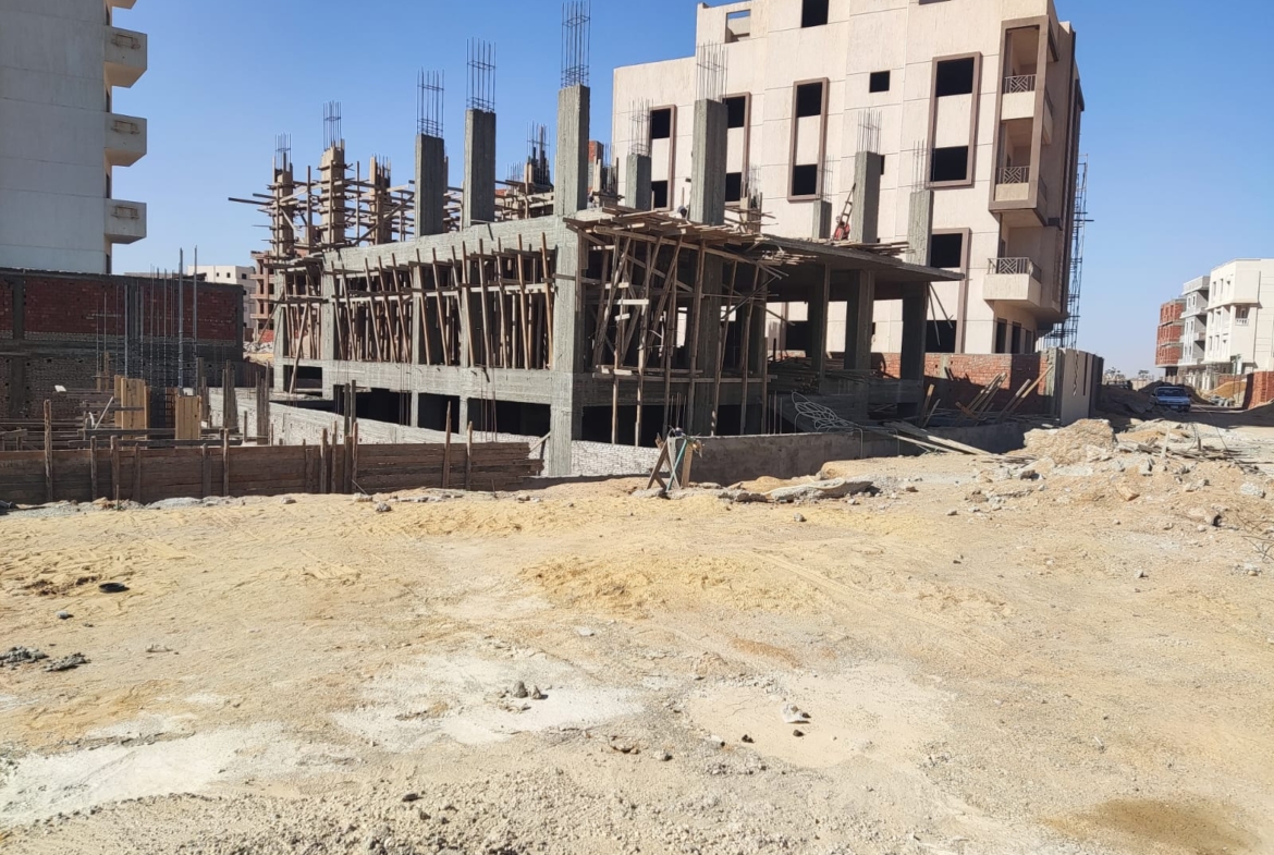 Construction site with a concrete frame and a white apartment building behind - apartment in Beit El Watan, New Cairo