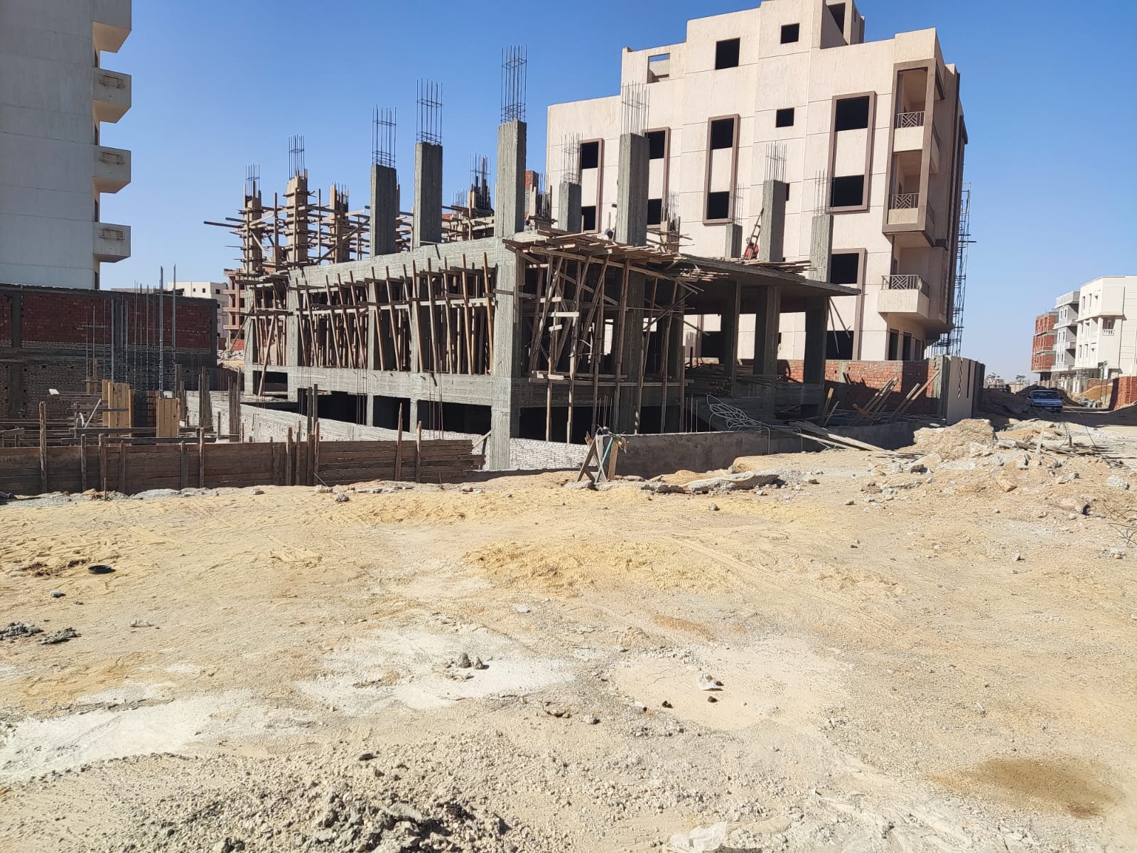 Construction site with a concrete frame and a white apartment building behind - apartment in Beit El Watan, New Cairo