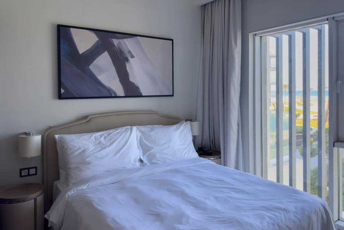 Bed with white linen and framed abstract art beside the balcony - hotel apartment in Marassi The Address Beach, North Coast