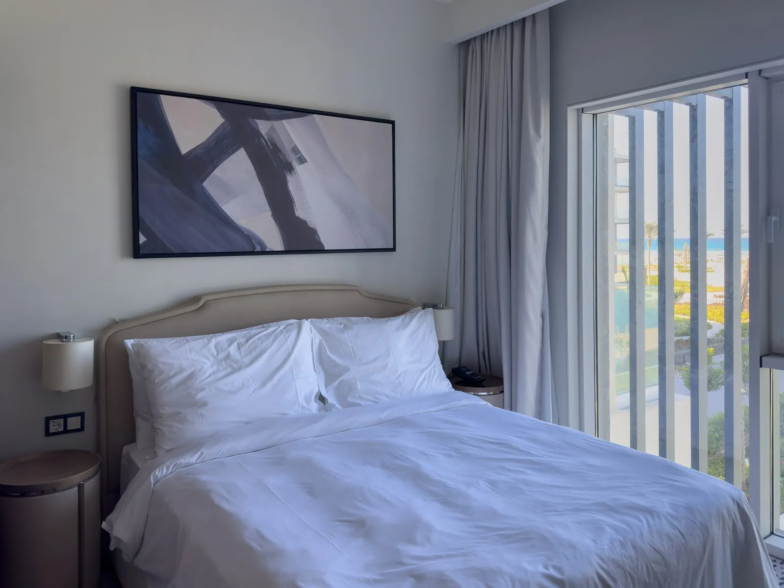 Bed with white linen and framed abstract art beside the balcony - hotel apartment in Marassi The Address Beach, North Coast