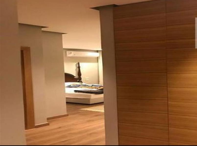 Bedroom seen past a wooden wall panel and a hallway - penthouse in Lake View, New Cairo