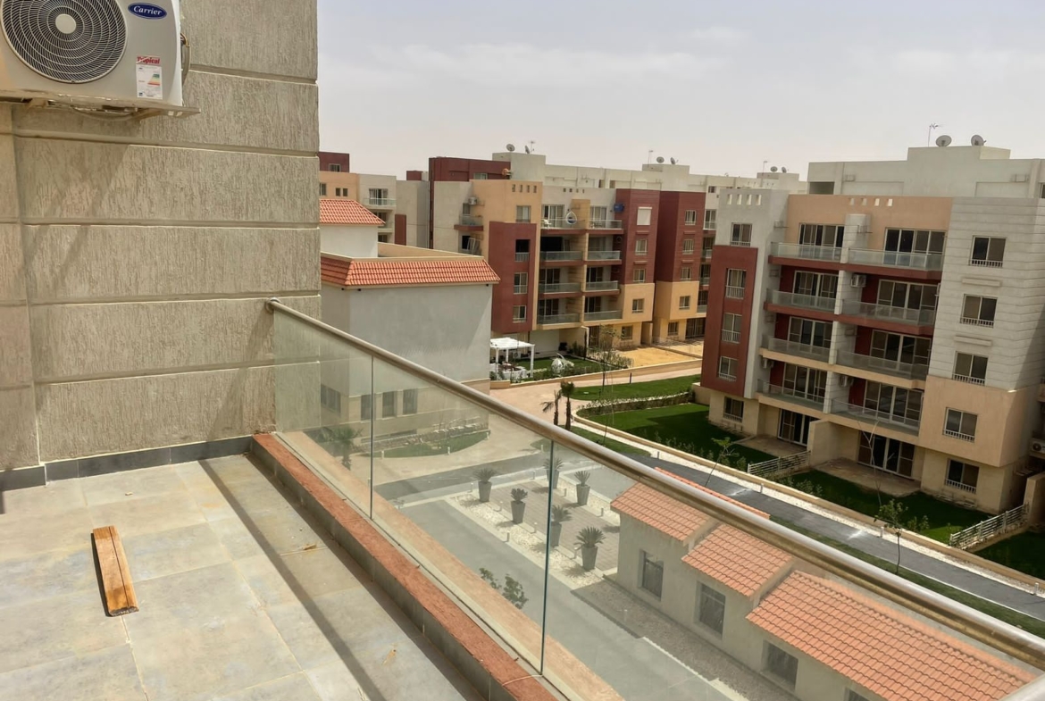 Glass-fenced balcony with an air conditioner and terracotta roofs below - penthouse in Promenade, New Cairo