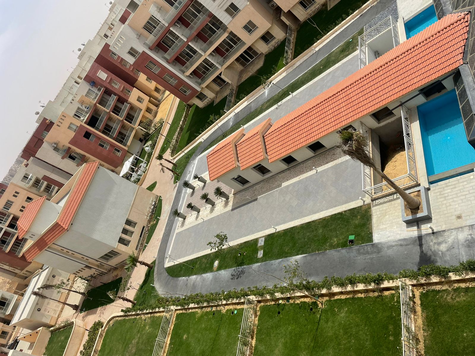 Top-down view of a terracotta roof strip, lawns and a pool corner - penthouse in Promenade, New Cairo