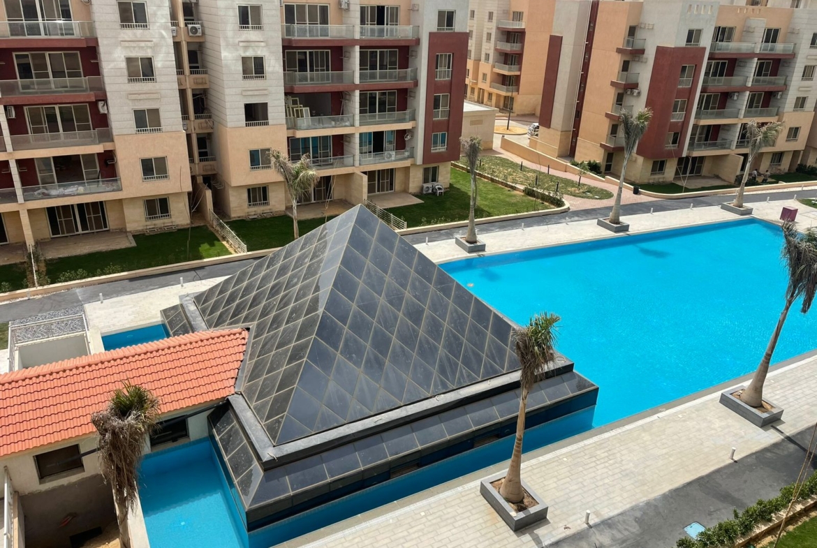 Pool with a glass pyramid roof and palm trees among apartment buildings - penthouse in Promenade, New Cairo