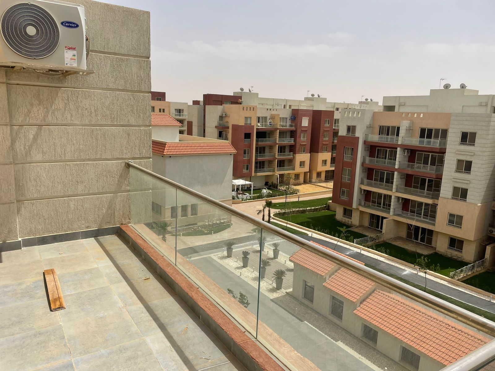 Balcony corner with a glass rail, an air conditioner and a view of the compound - penthouse in Promenade, New Cairo
