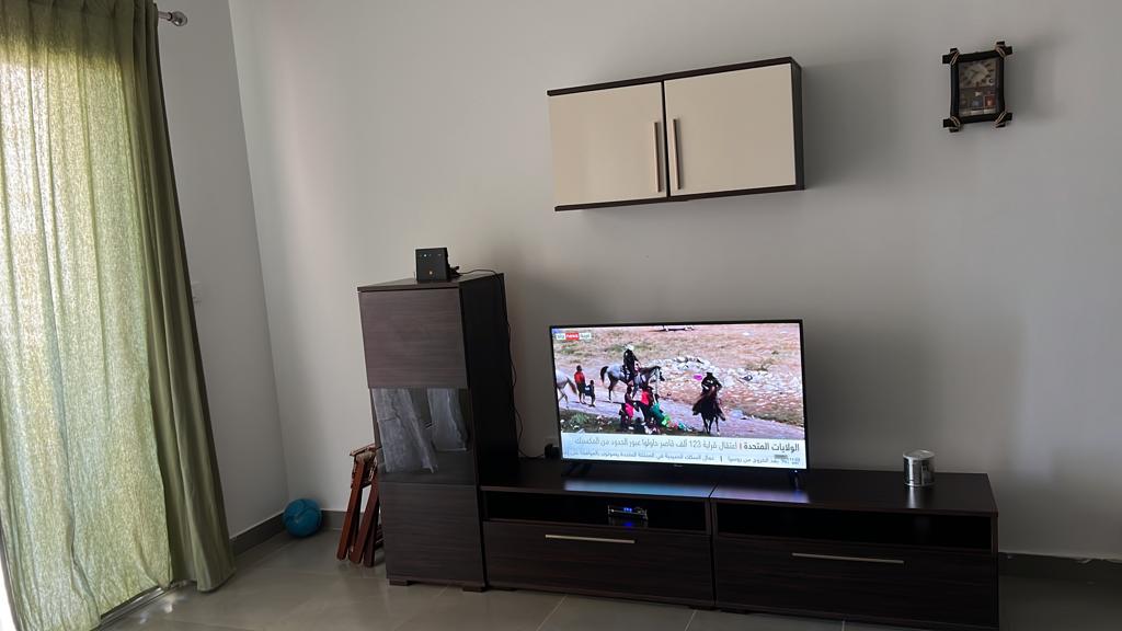 TV on a dark stand with a wall cabinet and green curtain - chalet in Amwaj, North Coast