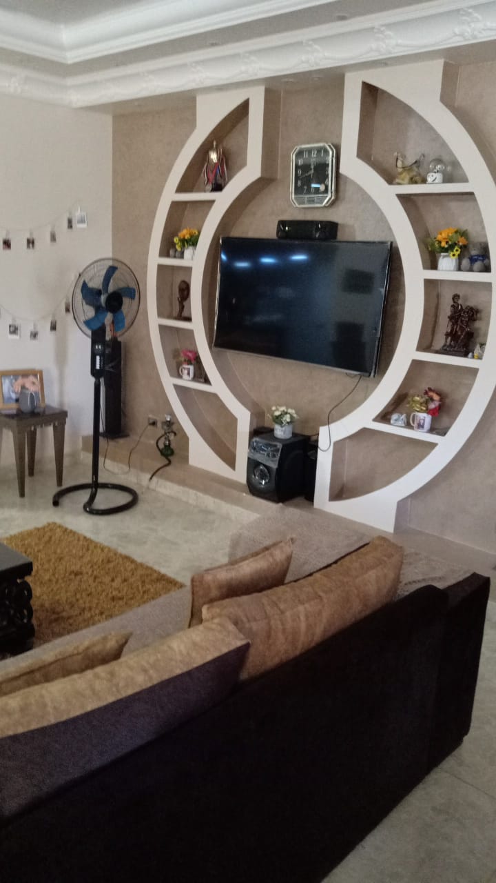 Living room with a round white TV unit and dark sofas - duplex in South of Academy, New Cairo