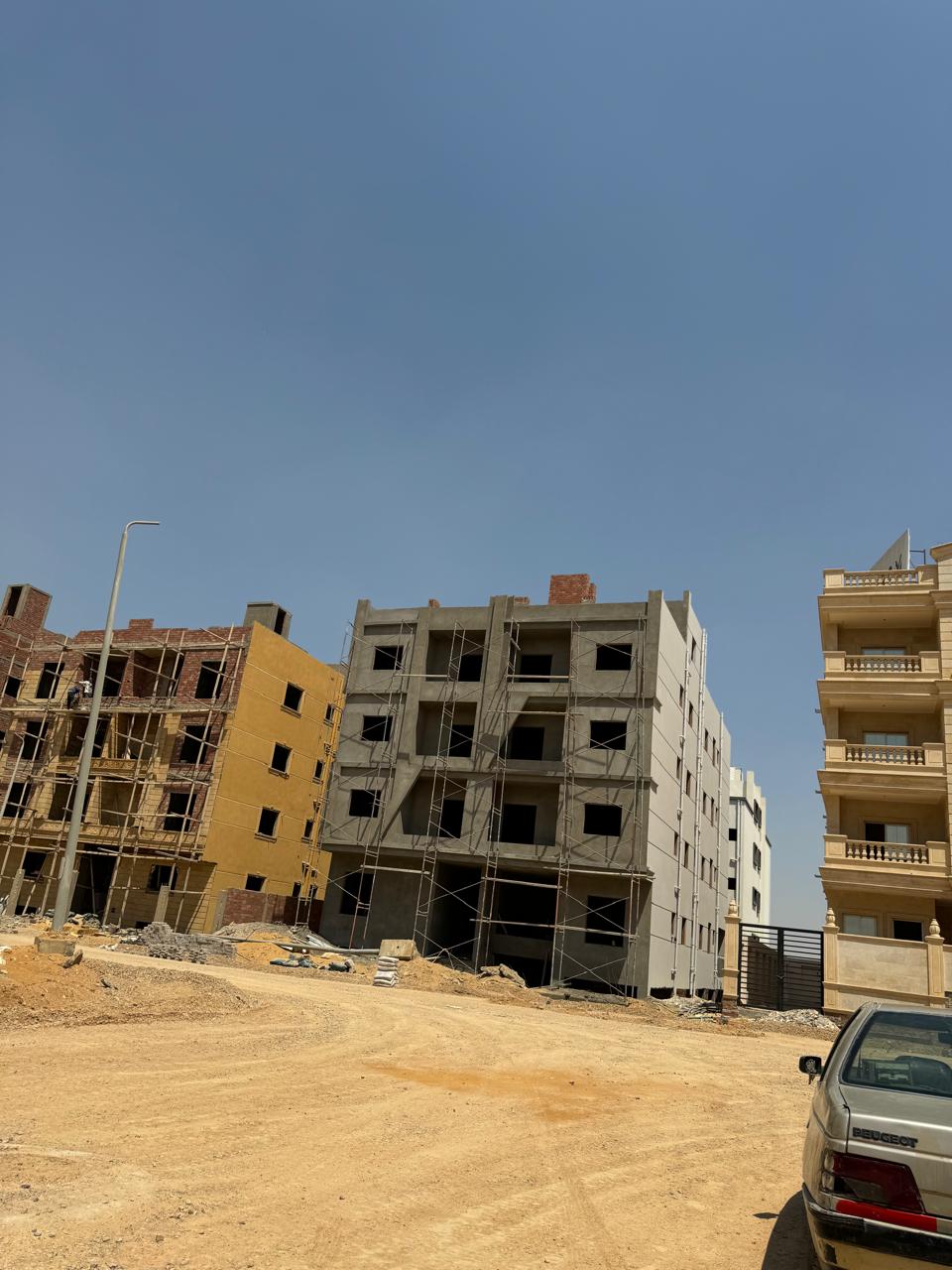 Residential blocks under construction beside a sandy street - apartment in Bayt Al Watan, New Cairo