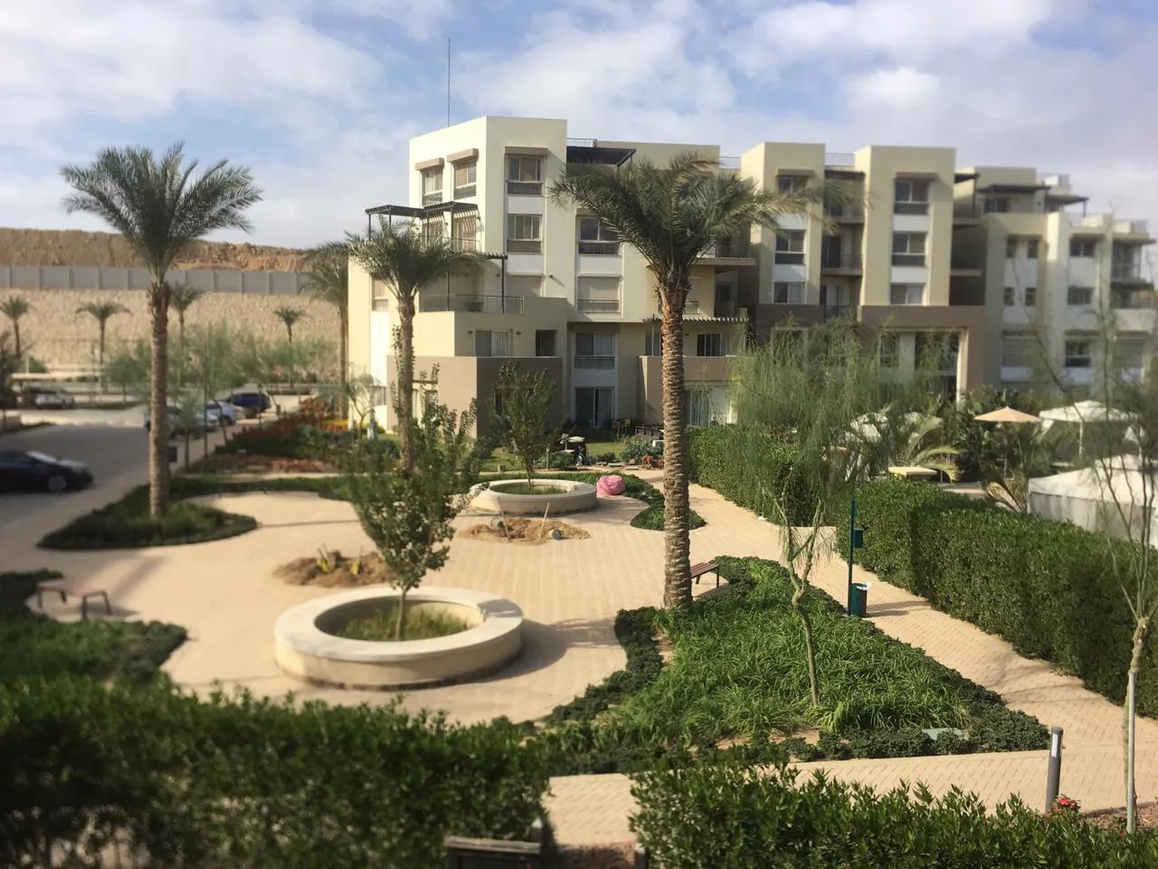 10-20261012-06-1145-source-36 فناء بنخيل وحوض زرع دائري وممشى مبلط بين المباني - دوبلكس في سييراز، القاهرة