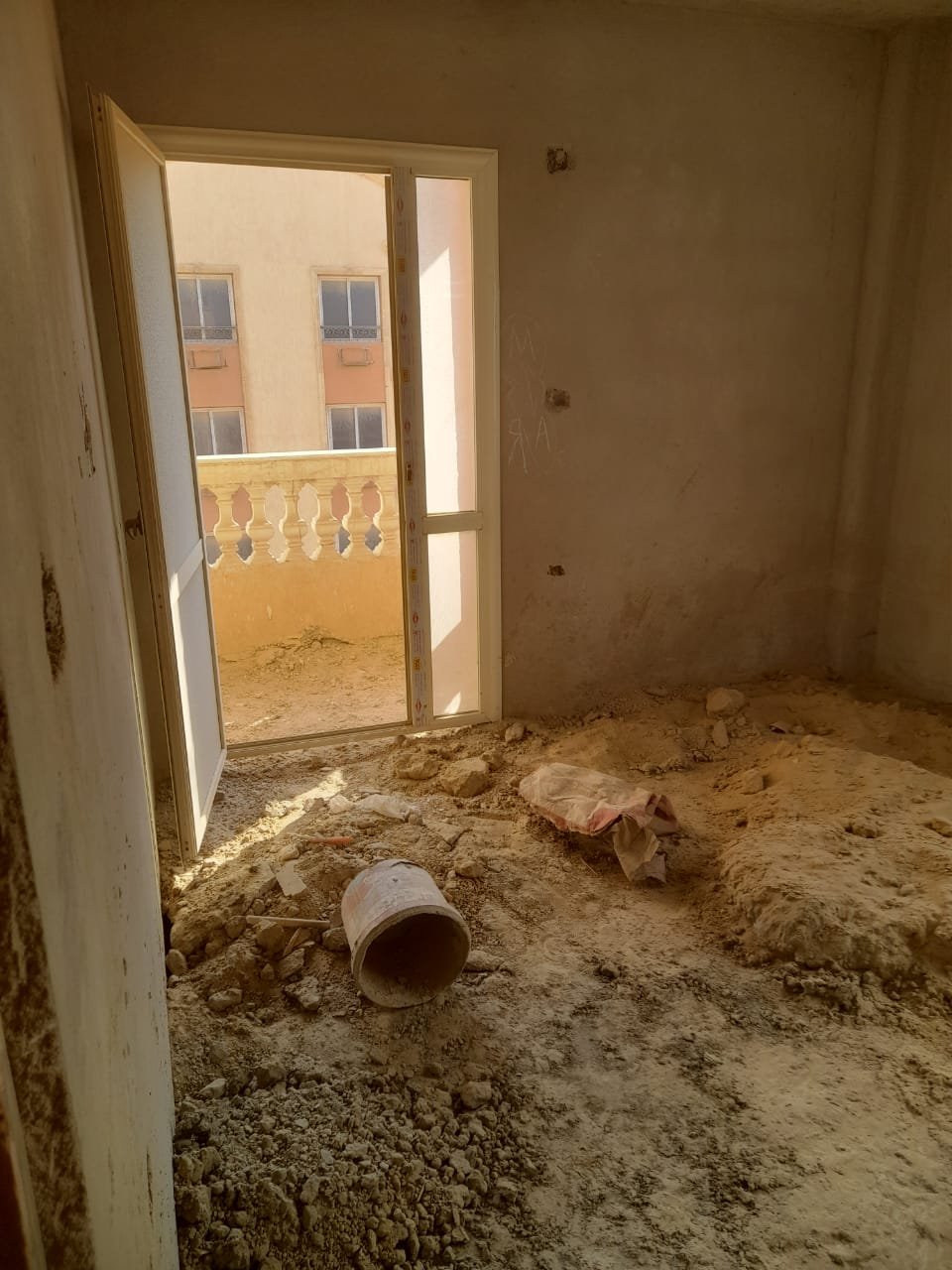 Unfinished room with a balcony door and a pipe on a sandy floor - penthouse in Green House, 5th Settlement