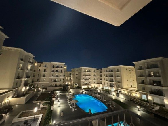 Pool and landscaped courtyard view at night, apartment for rent in Mivida Boulevard, New Cairo | إطلالة حمام السباحة واللاندسكيب ليلاً، شقة للإيجار في ميفيدا البوليفارد، القاهرة الجديدة