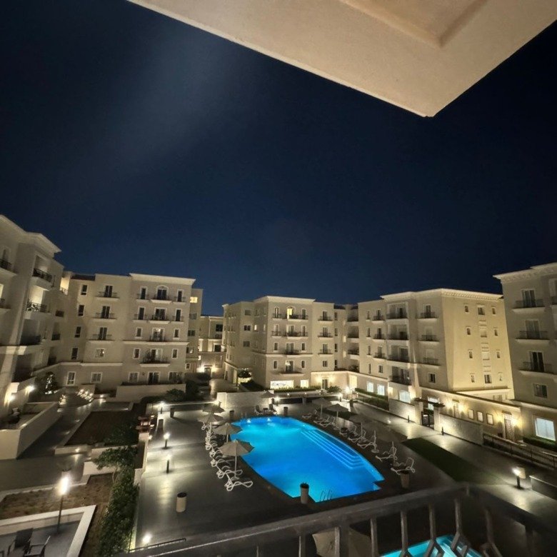 Pool and landscaped courtyard view at night, apartment for rent in Mivida Boulevard, New Cairo | إطلالة حمام السباحة واللاندسكيب ليلاً، شقة للإيجار في ميفيدا البوليفارد، القاهرة الجديدة