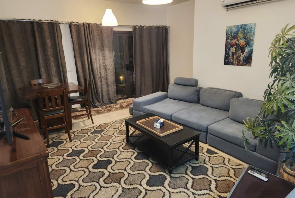 Living room with grey sofa and wooden dining table - apartment in Golden Square, Fifth Square, New Cairo