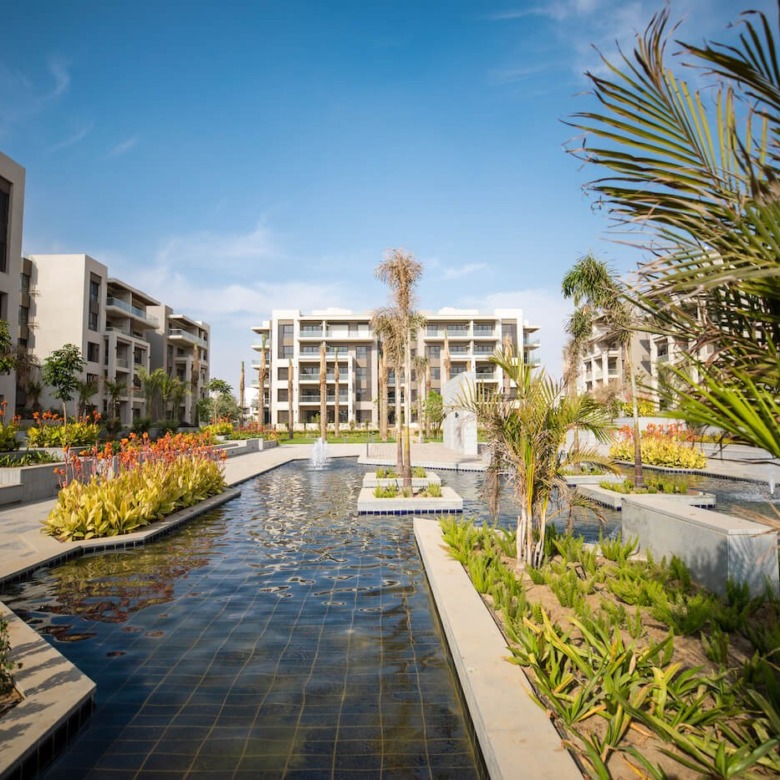 Water features and gardens between buildings, The Address East, New Cairo - general project photo for apartment for sale | مساحات مائية وحدائق بين المباني، ذا أدريس إيست، القاهرة الجديدة - صورة عامة للمشروع لشقة للبيع
