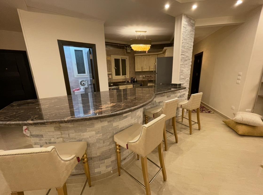 akoya-513-1 Open kitchen with a granite breakfast bar and cream stools - apartment in Akoya, New Cairo