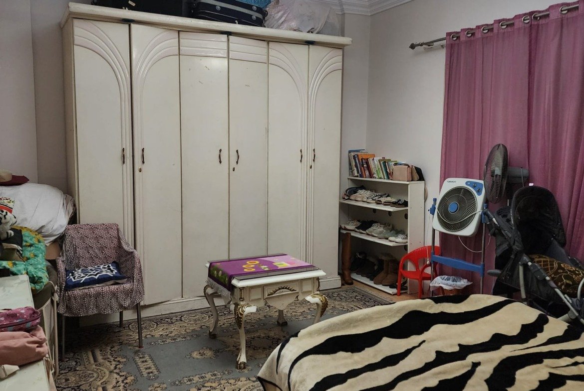 Bedroom with a tall white wardrobe and a striped bed cover - apartment in Al Narges, New Cairo