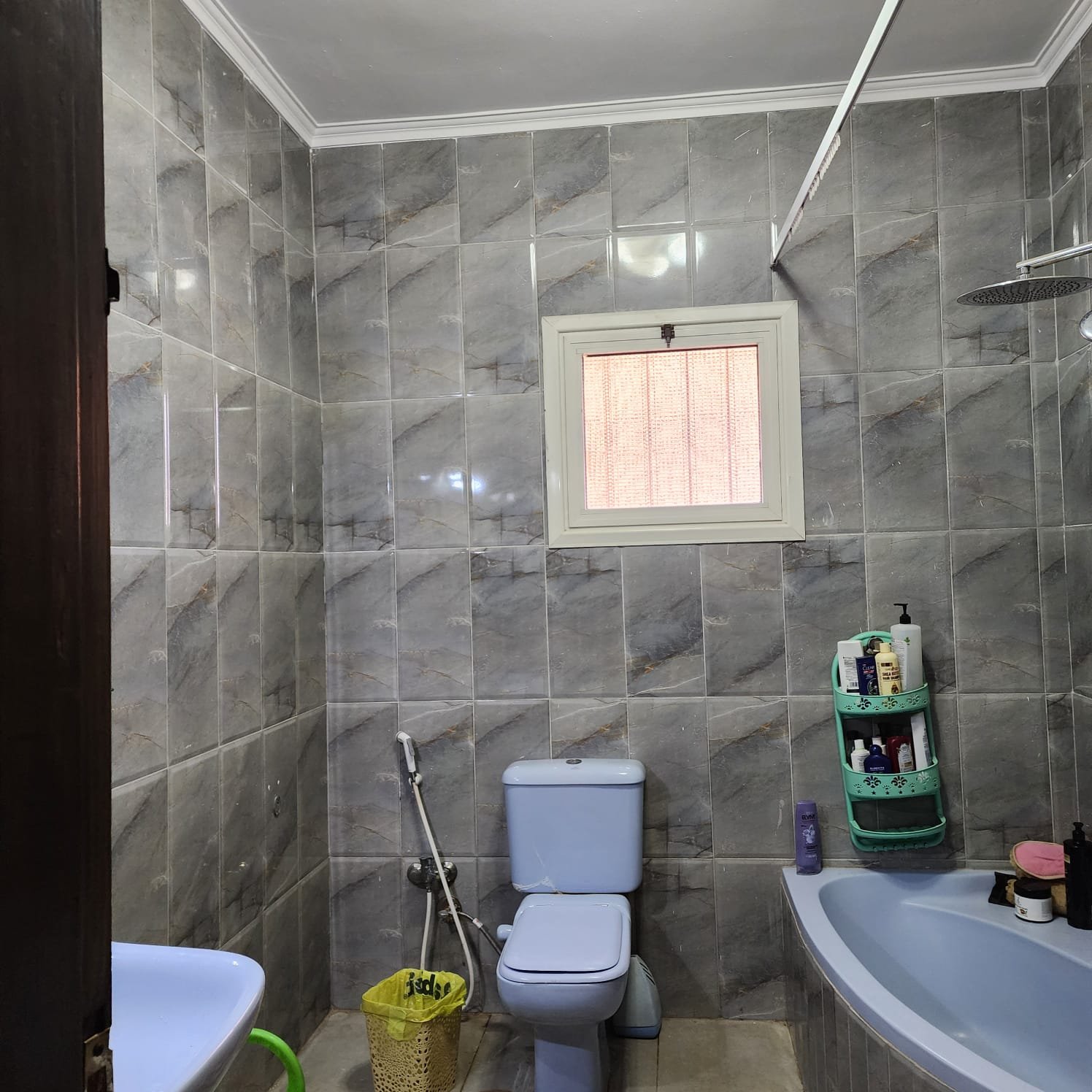 Bathroom with grey wall tiles, a corner bathtub and a small window - apartment in Al Narges, New Cairo