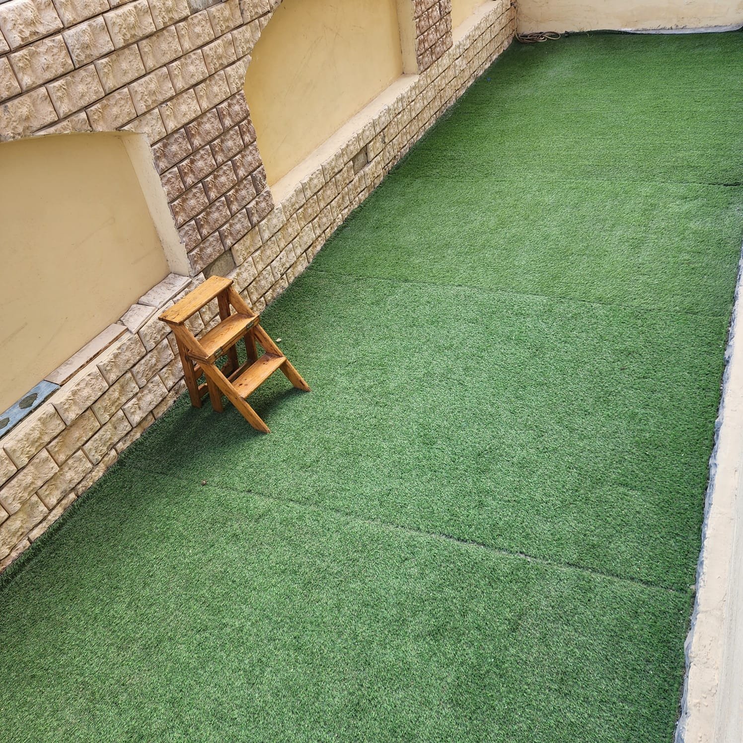 Strip of artificial grass with a small wooden step ladder - apartment in Al Narges, New Cairo