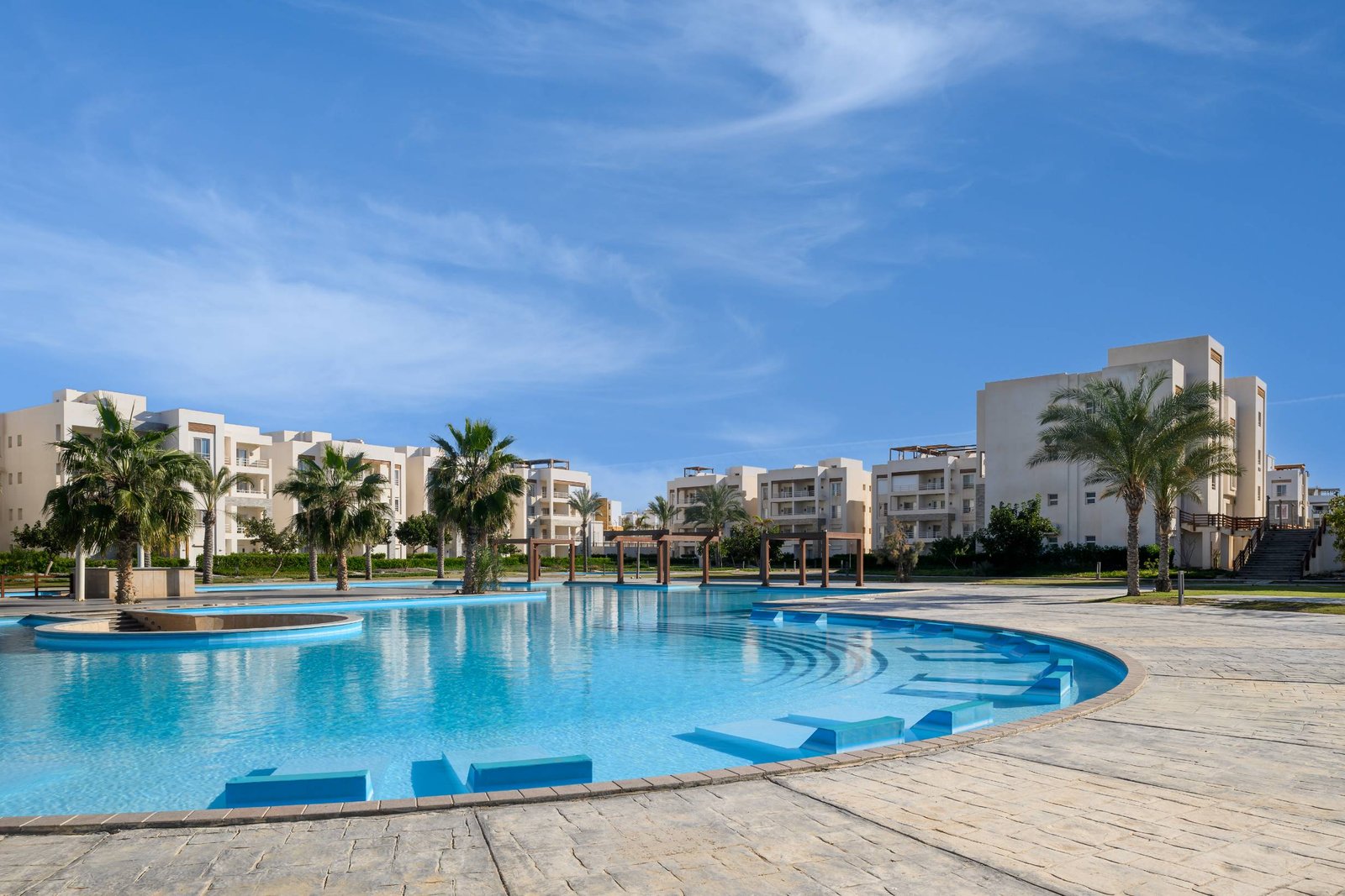 Wide curved pool with sun beds and low-rise buildings - chalet in Amwaj, North Coast