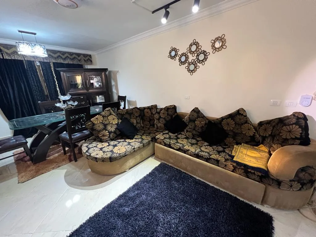 Living room with a floral corner sofa and a navy rug - apartment in Dar Misr Al Andalus, 5th Settlement