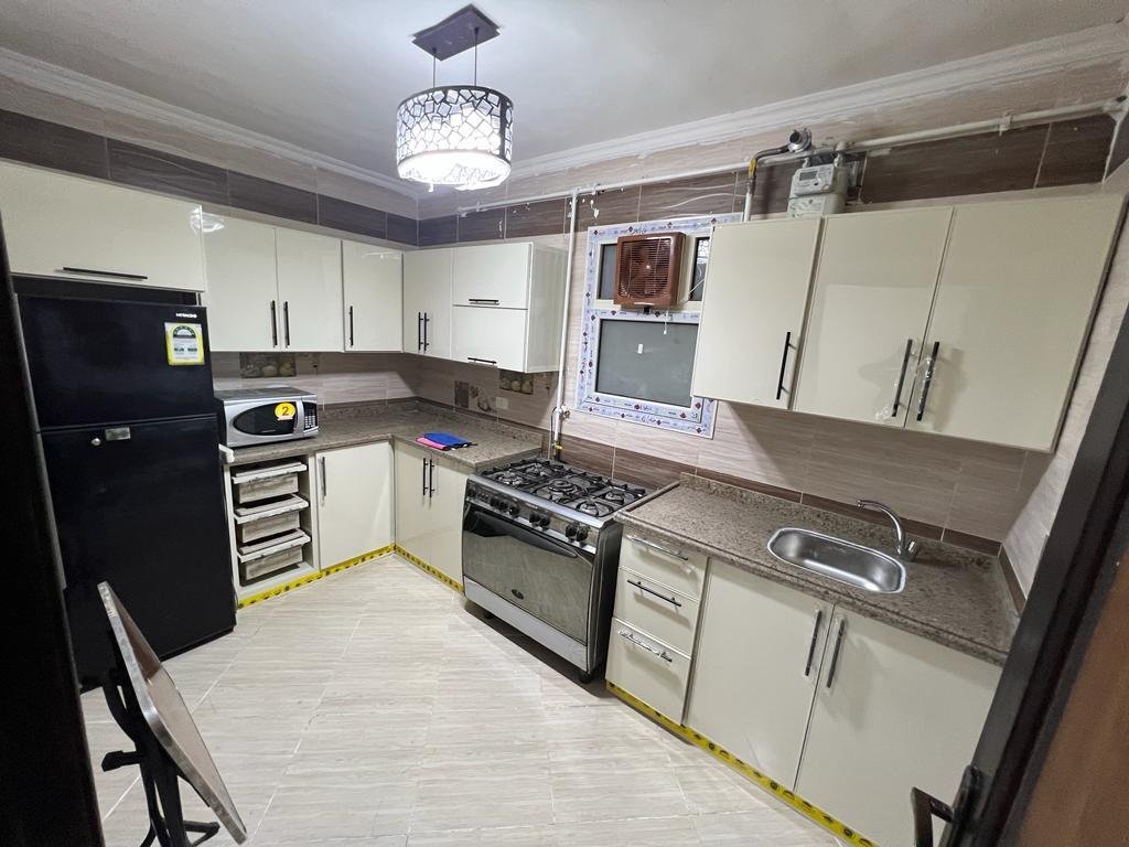 Kitchen with cream cabinets, a gas cooker and a black fridge - apartment in Dar Misr Al Andalus, 5th Settlement