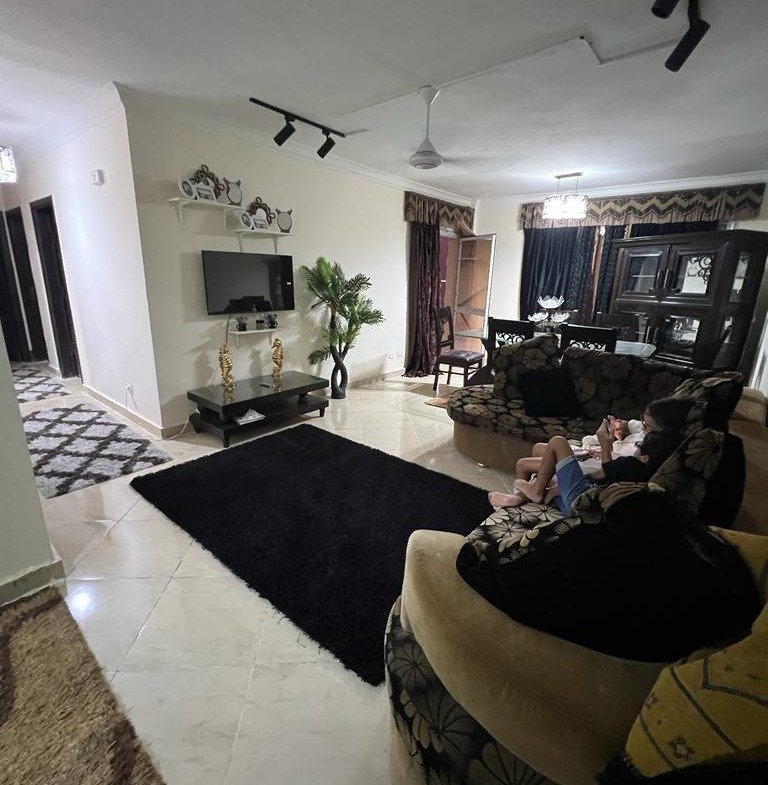 Living room with a dark rug, a wall TV and a curved sofa seen from the entrance - apartment in Dar Misr Al Andalus, 5th Settlement