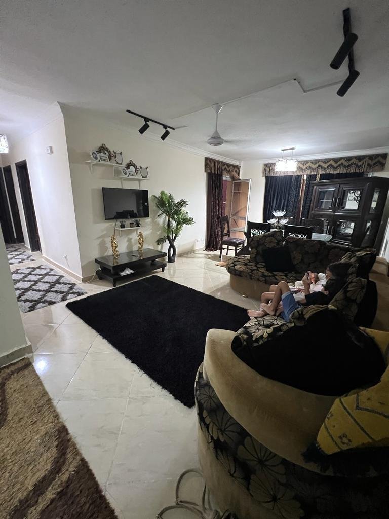 Living room with a dark rug, a wall TV and a curved sofa seen from the entrance - apartment in Dar Misr Al Andalus, 5th Settlement