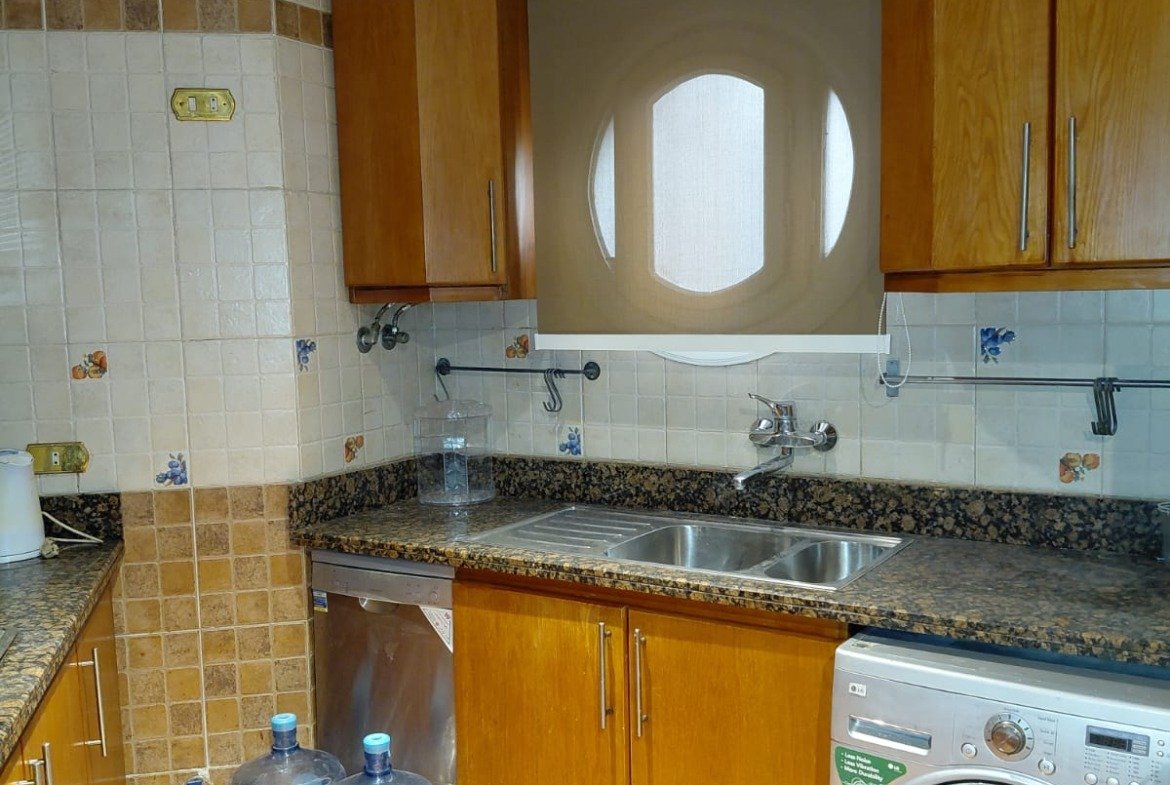 Kitchen with wooden cabinets, a washing machine and water bottles - villa in El Yasmeen 1 Villas, New Cairo