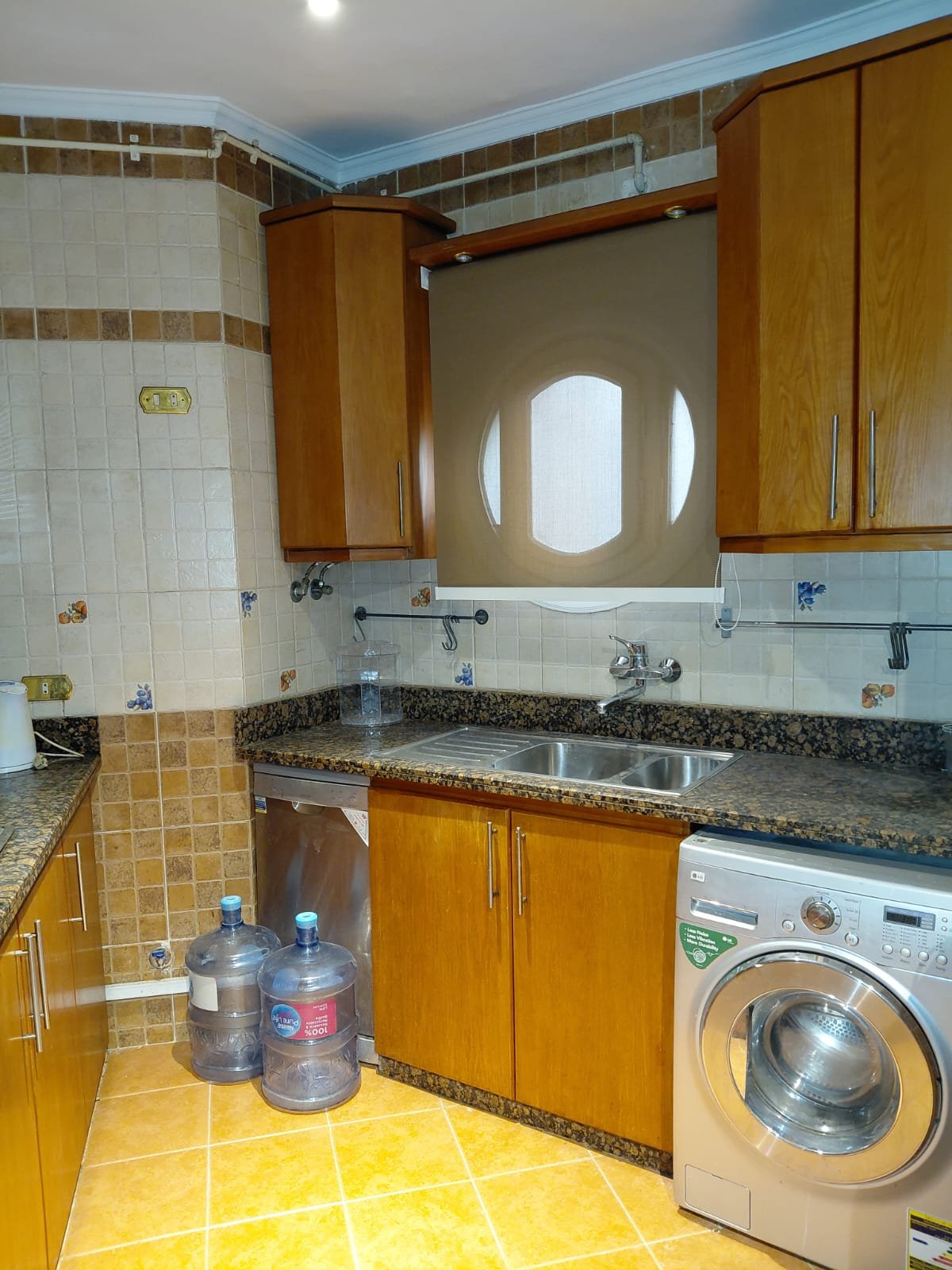 Kitchen with wooden cabinets, a washing machine and water bottles - villa in El Yasmeen 1 Villas, New Cairo