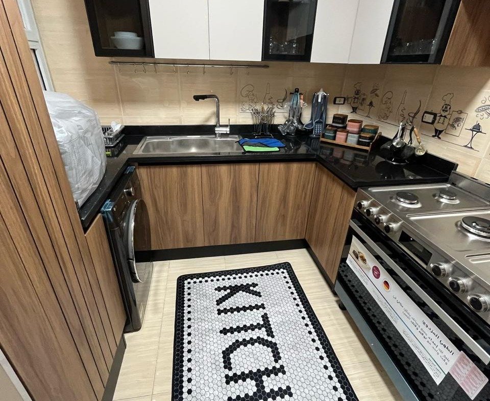 Kitchen with wooden cabinets and a lettered floor mat - apartment in Eazy Life, New Cairo
