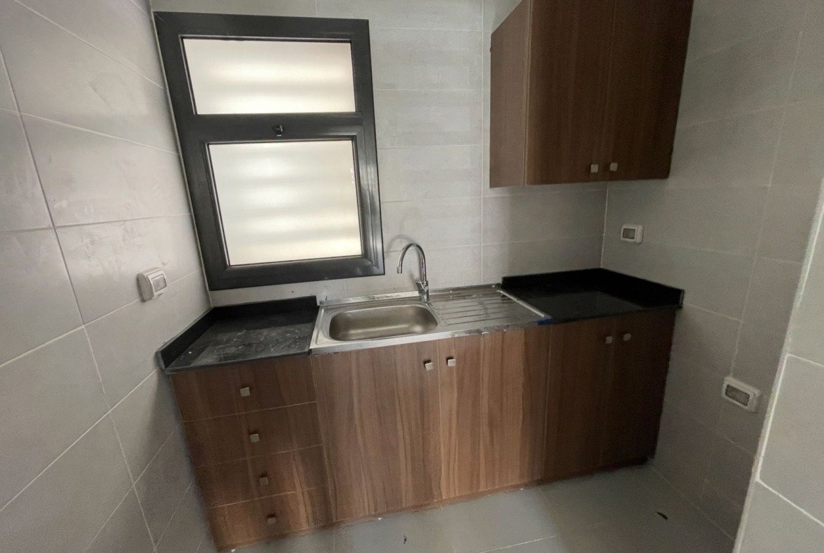 Small kitchen unit with a steel sink and wood cabinets - apartment in Privado, New Cairo