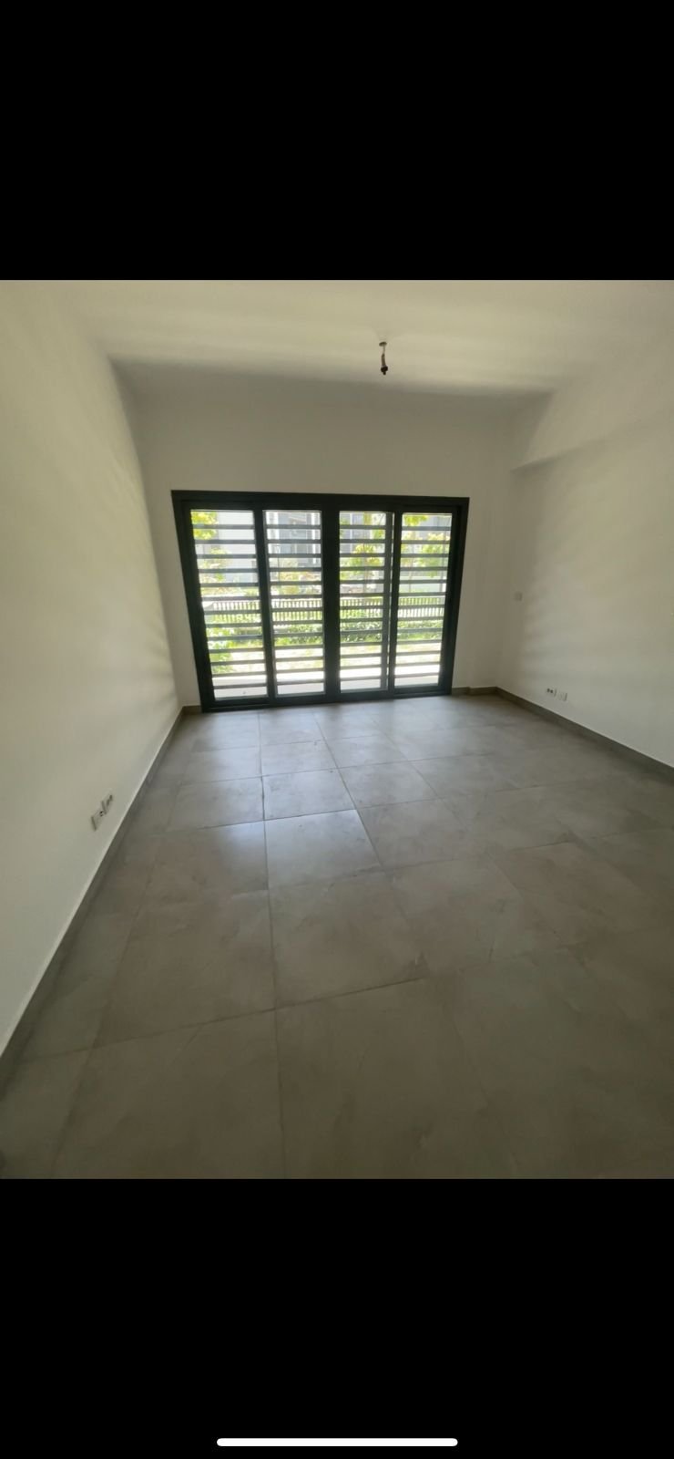 Room with a wide window and a grey floor - apartment in Privado, New Cairo
