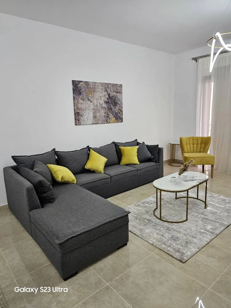 apartment-moon-residences-5th-square-new-cairo-167-sqm-397-living-room غرفة معيشة بأريكة ركنية داكنة وكراسي صفراء - شقة في مون ريزيدنس فيفث سكوير، القاهرة الجديدة