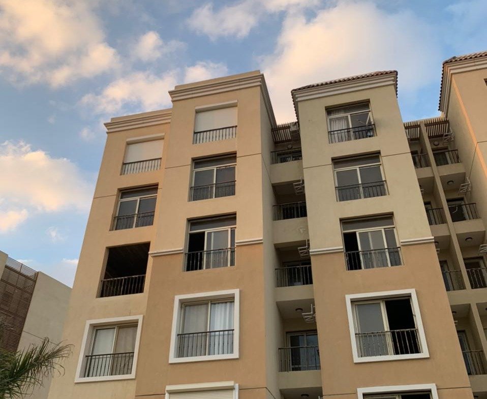 Cream and orange apartment building seen from below under a cloudy sky - apartment in Sarai, Mostaqbal City