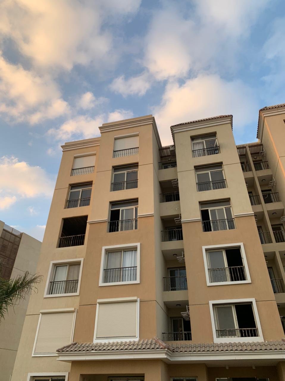 Cream and orange apartment building seen from below under a cloudy sky - apartment in Sarai, Mostaqbal City