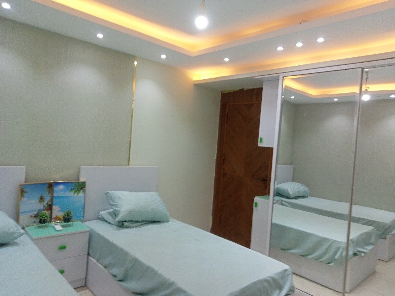Twin-bed room with mint bedding and a mirrored wardrobe - apartment in Sarai, Mostaqbal City