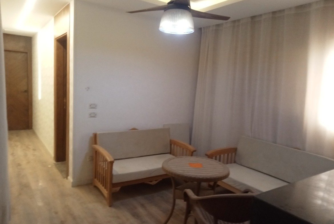 Compact living room with a ceiling fan, a wooden sofa and a round table - apartment in Sarai, Mostaqbal City