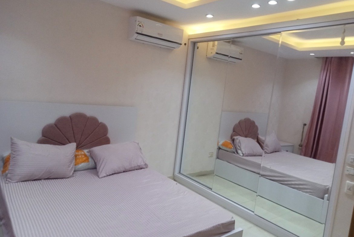 Bedroom with a pink headboard, a mirrored wardrobe and a split air conditioner - apartment in Sarai, Mostaqbal City