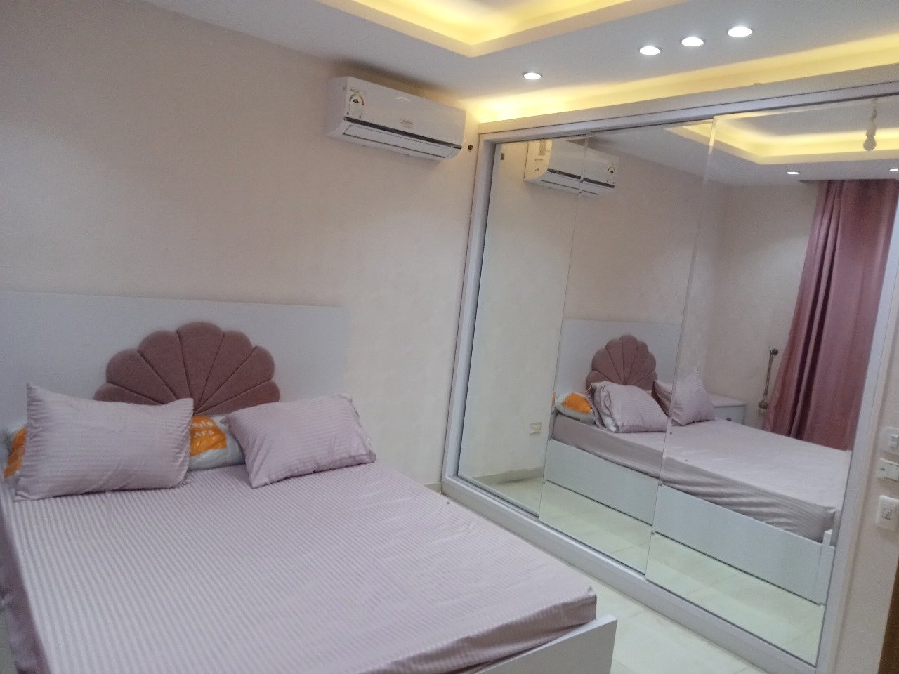 Bedroom with a pink headboard, a mirrored wardrobe and a split air conditioner - apartment in Sarai, Mostaqbal City