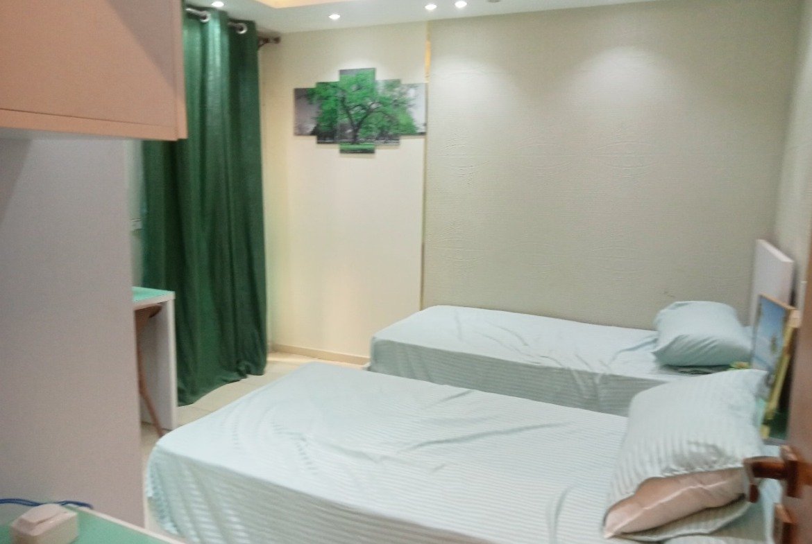 Twin-bed room with mint bedding and green curtains - apartment in Sarai, Mostaqbal City