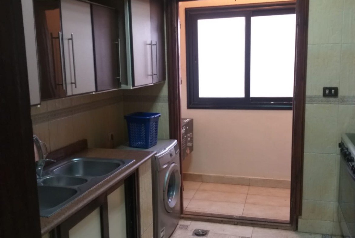 Kitchen with dark wooden cabinets and a balcony door - apartment in Yasmeen 3, New Cairo