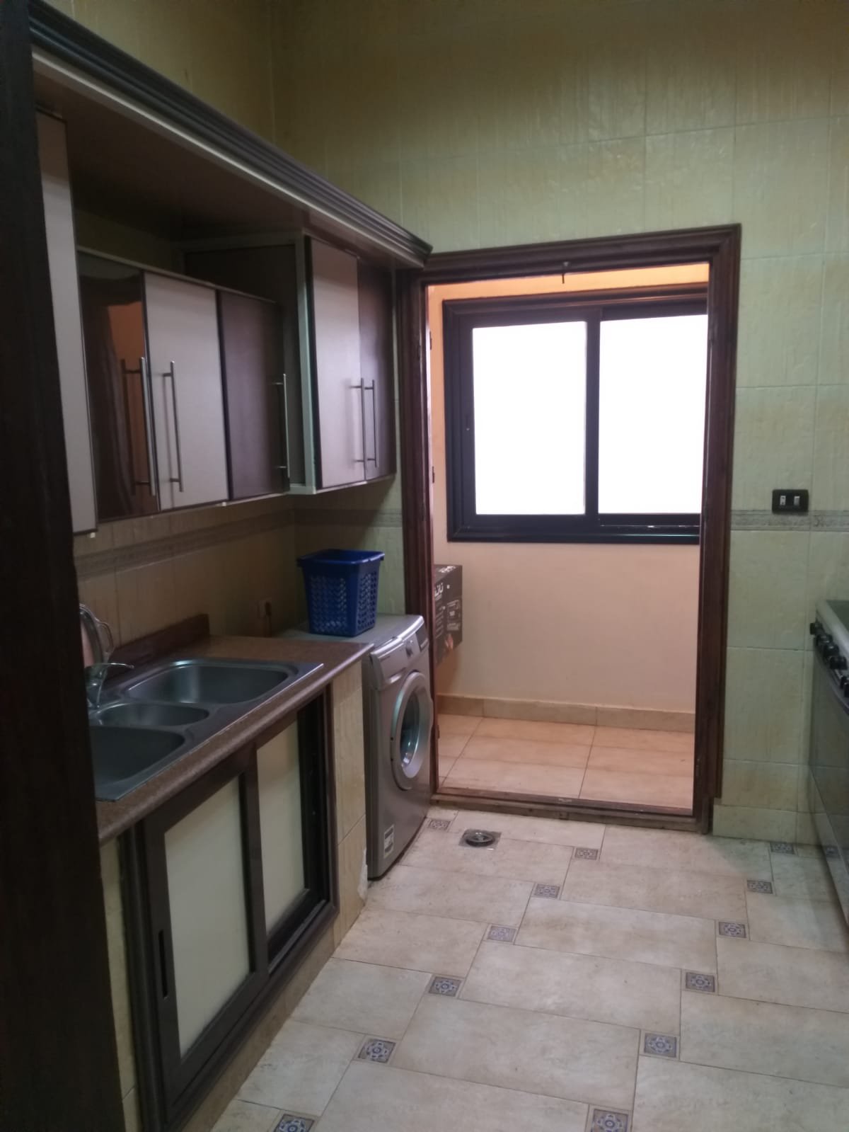 Kitchen with dark wooden cabinets and a balcony door - apartment in Yasmeen 3, New Cairo