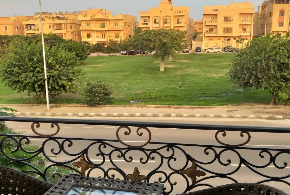 Balcony with a small table and chairs overlooking a green lawn - apartment in Yasmeen 3, New Cairo