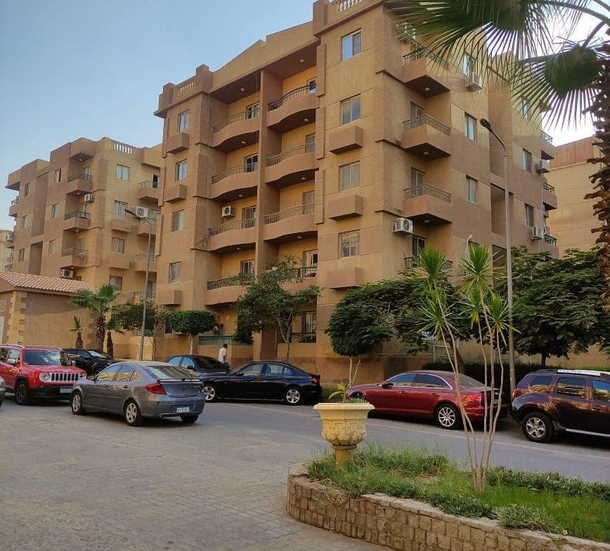 Apartment buildings behind a parking area and a planted corner - apartment in Ashrafeya Residence, New Cairo