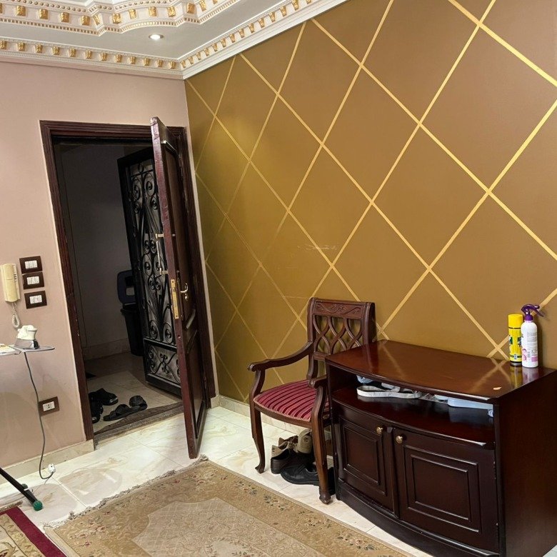 Entry with a gold diamond-pattern wall and a wooden cabinet - apartment in Banafseg Buildings, New Cairo